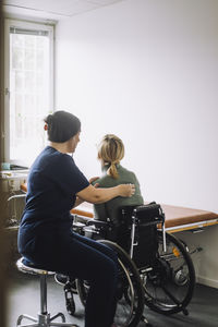 Side view of female nurse examining woman sitting on wheelchair in clinic