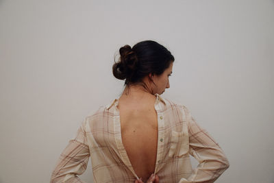 Rear view of woman buttoning shirt against white background