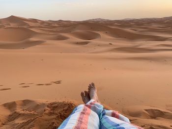 Low section of woman siting on sand dune at desert against sky