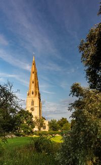 Low angle view of church clock tower amidst trees and buildings against sky