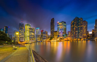 Illuminated buildings by river against sky in city at night