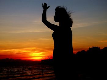 Silhouette woman standing by sea against sky during sunset