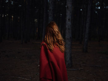 Rear view of woman standing by tree trunk in forest