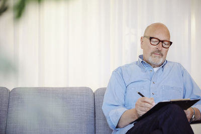 Confident senior therapist writing on clipboard at wellness center