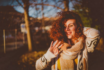 Smiling young woman standing against trees during sunny day