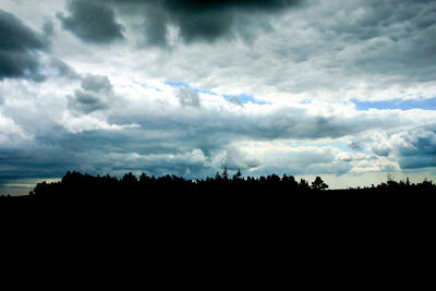 Silhouette trees on landscape against dramatic sky