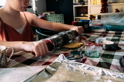 Teen girl rolling out cookie dough at dining room table