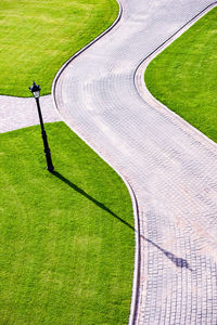 Cobbled park alleys surrounded by green grass on a sunny, bright spring day. lamp shade visible.