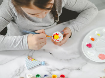 Little caucasian girl enthusiastically paints an easter egg with a brush of red-yellow acrylic paint