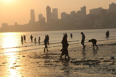 Silhouette people at beach against sky during sunset