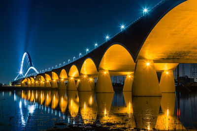 Illuminated bridge over river against sky at night