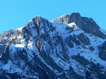 Low angle view of snowcapped mountains against clear blue sky