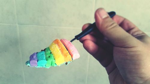 Cropped image of person holding colorful cake on spoon against wall