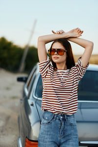 Portrait of young woman wearing sunglasses while standing against car