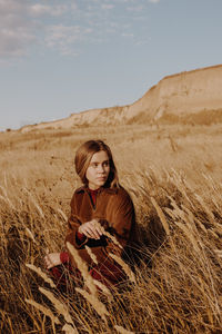 Young woman looking away while sitting by plants against sky