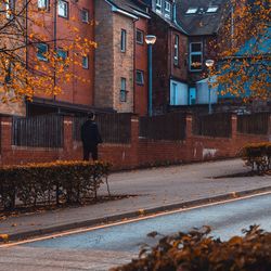 Rear view of man on street by buildings during autumn