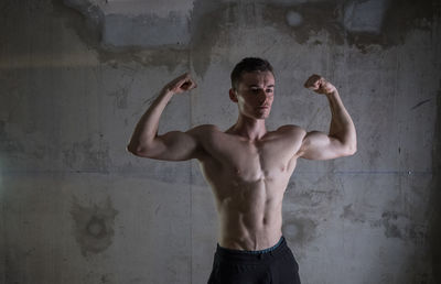 Young man flexing muscles against wall