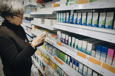 Senior female customer examining medicine standing by rack at pharmacy store