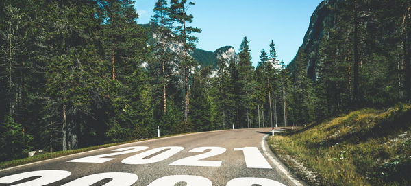 Road sign by trees against sky