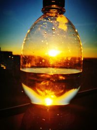 Close-up of glass bottle against sky during sunset