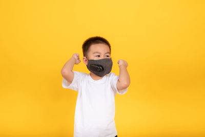 Full length portrait of boy standing against yellow background