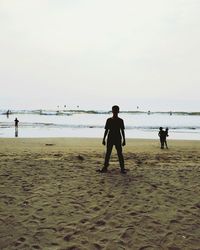 Rear view of silhouette people walking on beach against clear sky