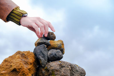 Cropped hand of man stacking rocks against sky