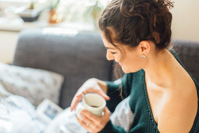 Close-up of woman having coffee while sitting on bed at home