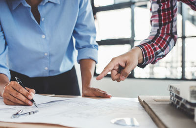 Midsection of architects working over blueprint on table