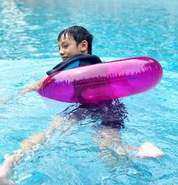 Smiling boy with inflatable ring swimming in pool