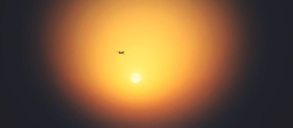Low angle view of silhouette airplane against orange sky