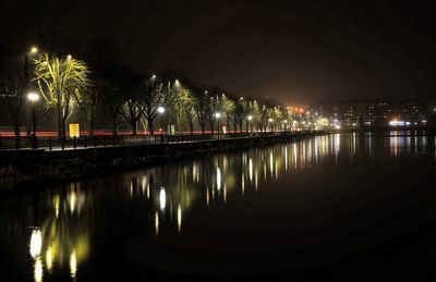 Illuminated city by river against sky at night