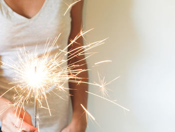 Midsection of woman holding lit sparkler against wall during christmas