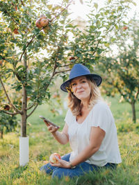 Young woman using phone while standing on plants