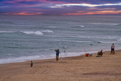 People on beach against sky during sunset