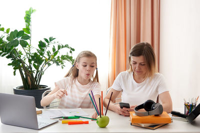 Mother and daughter sitting by desk at home