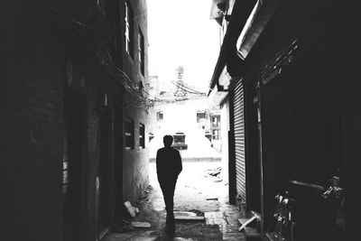 Rear view of man walking on street amidst buildings