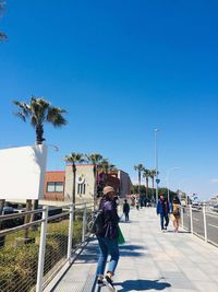 Full length of woman running on footpath in city against clear blue sky