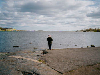 Rear view of girl standing by lake against cloudy sky