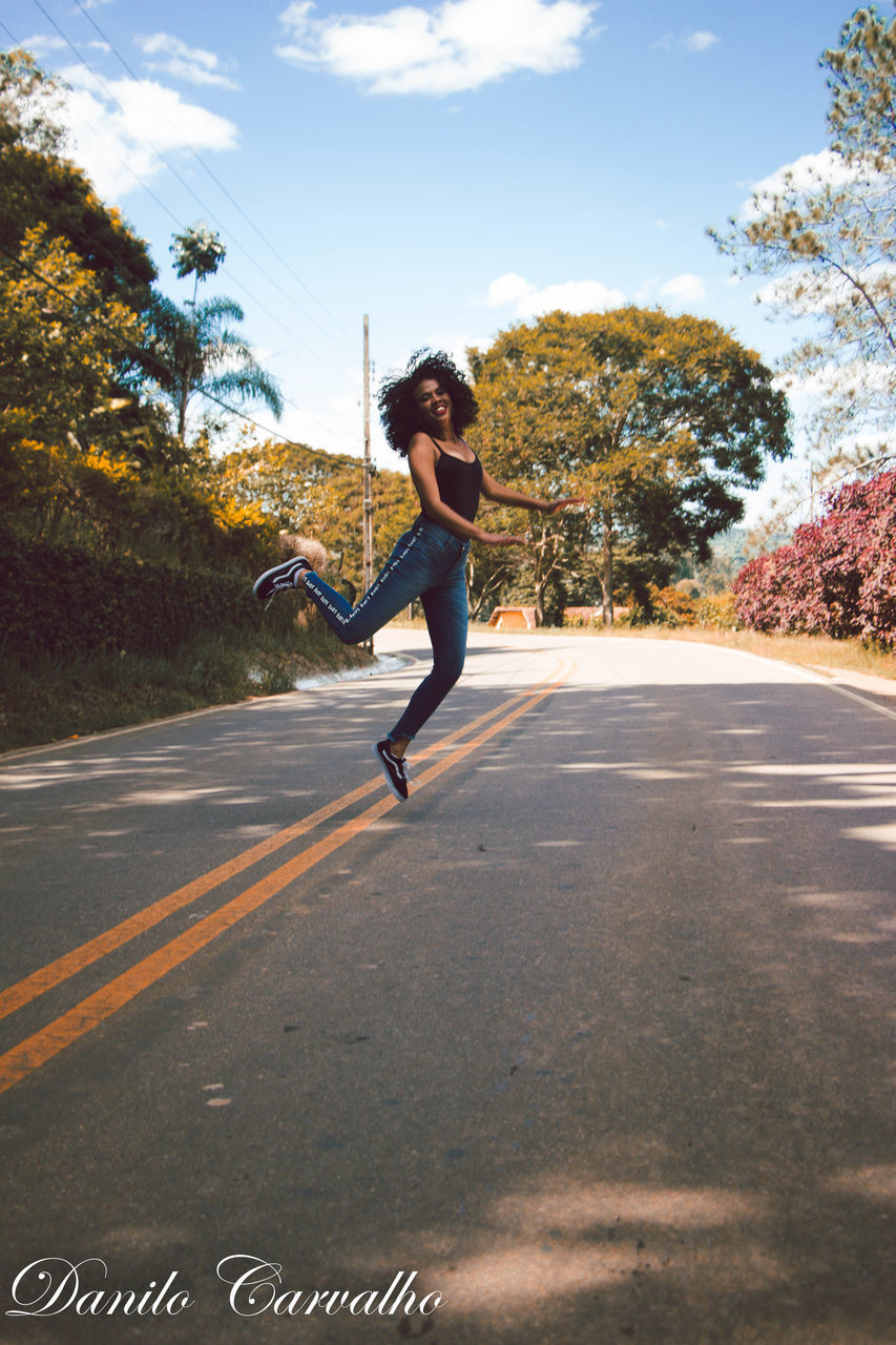 WOMAN JUMPING ON ROAD AGAINST SKY