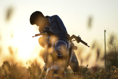 Young man with motorcycle on field against sky during sunset