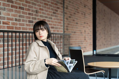 Young woman using mobile phone while standing against wall