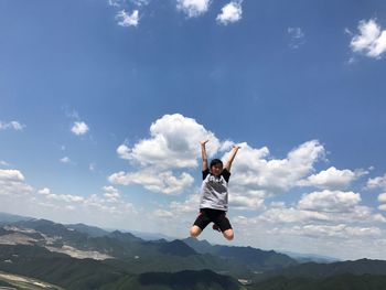 Girl with arms raised jumping against sky during sunny day