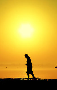 Silhouette woman walking at beach against orange sky