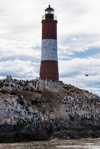 Lighthouse amidst rocks and buildings against sky