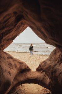 Rear view of woman standing at beach seen through rocks