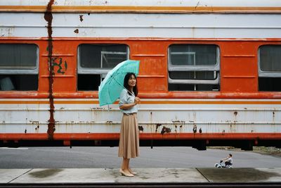 Side view of woman with umbrella standing at railroad station