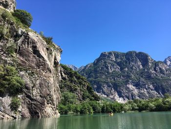 Scenic view of rocky mountains by sea against clear blue sky