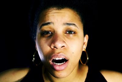 Portrait of young woman wearing earrings against black background