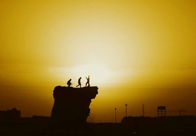 Silhouette people on cliff against sky during sunset